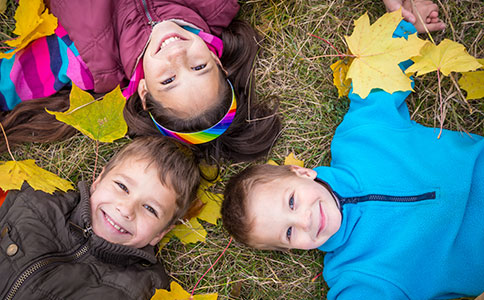 Tre børn ligger på græsset om efteråret