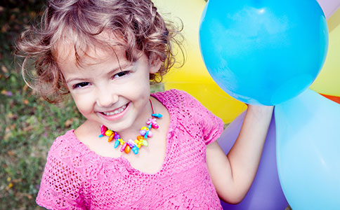 Glad pige står og holder farverige balloner